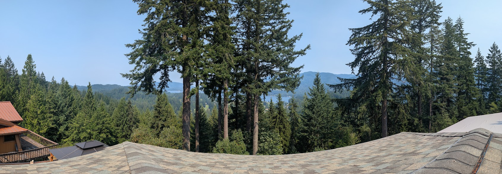 Panoramic view from a Sudden Valley rooftop over tall fir trees to Lake Whatcom and the hills